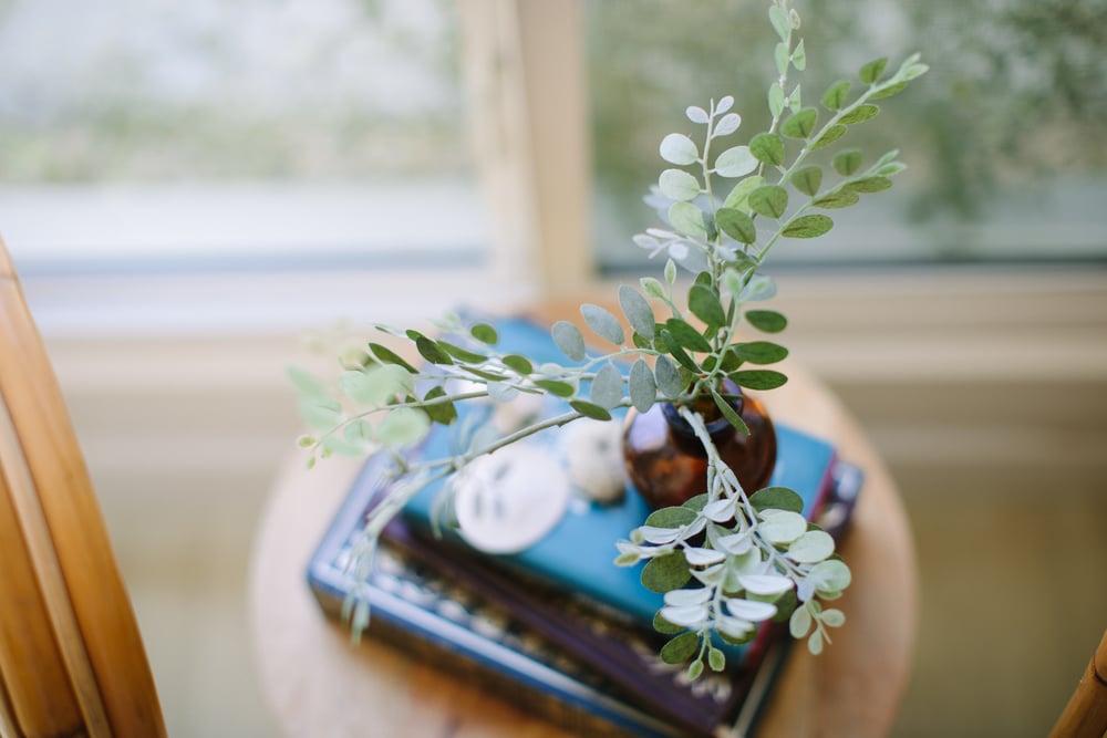A quiet side table with eucalyptus, a teal notebook, and a book — the feel of handling a few minutes of paperwork at home.