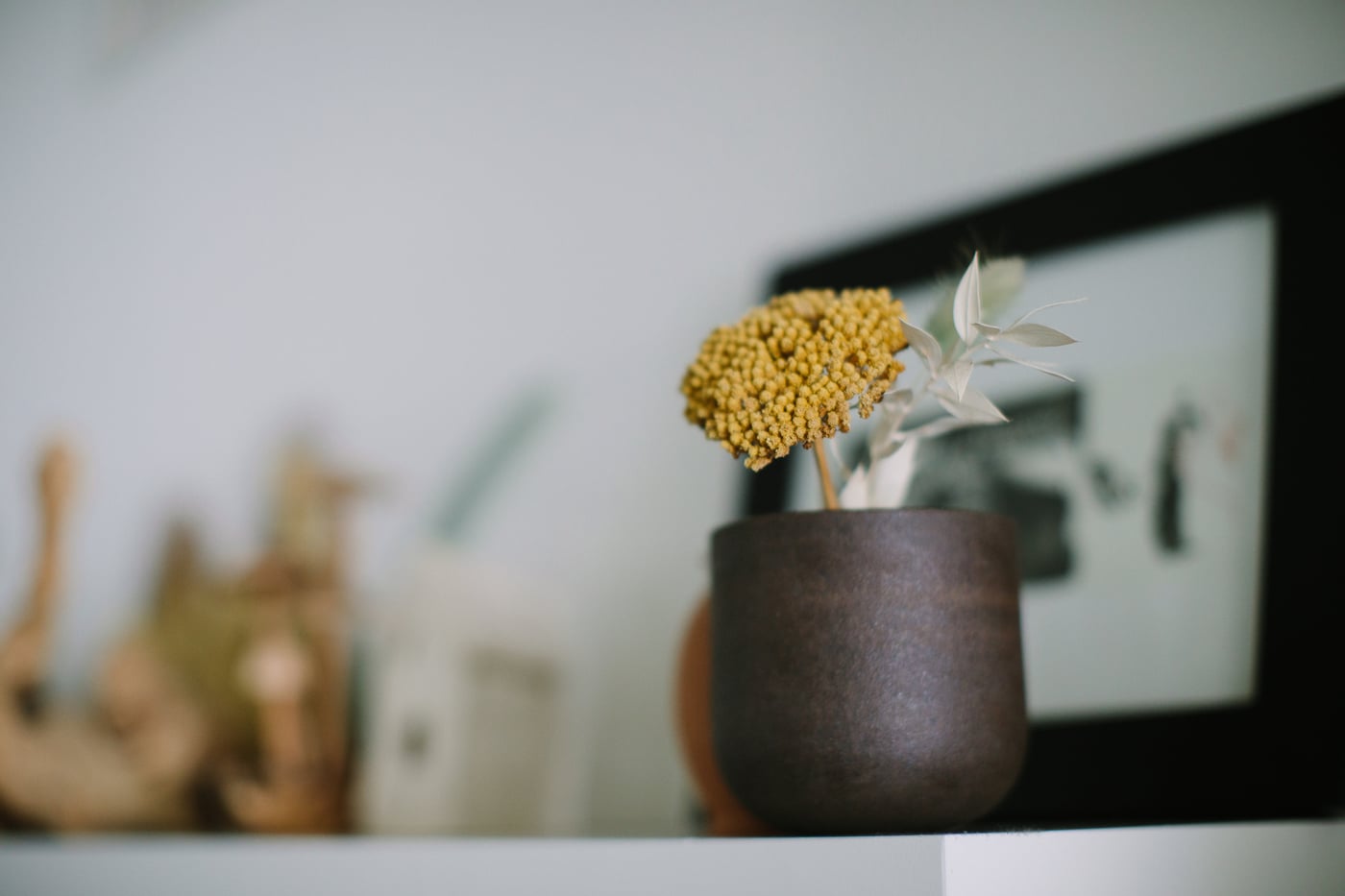 A dried yellow flower in a small brown vase on a shelf — a quiet moment of detail.