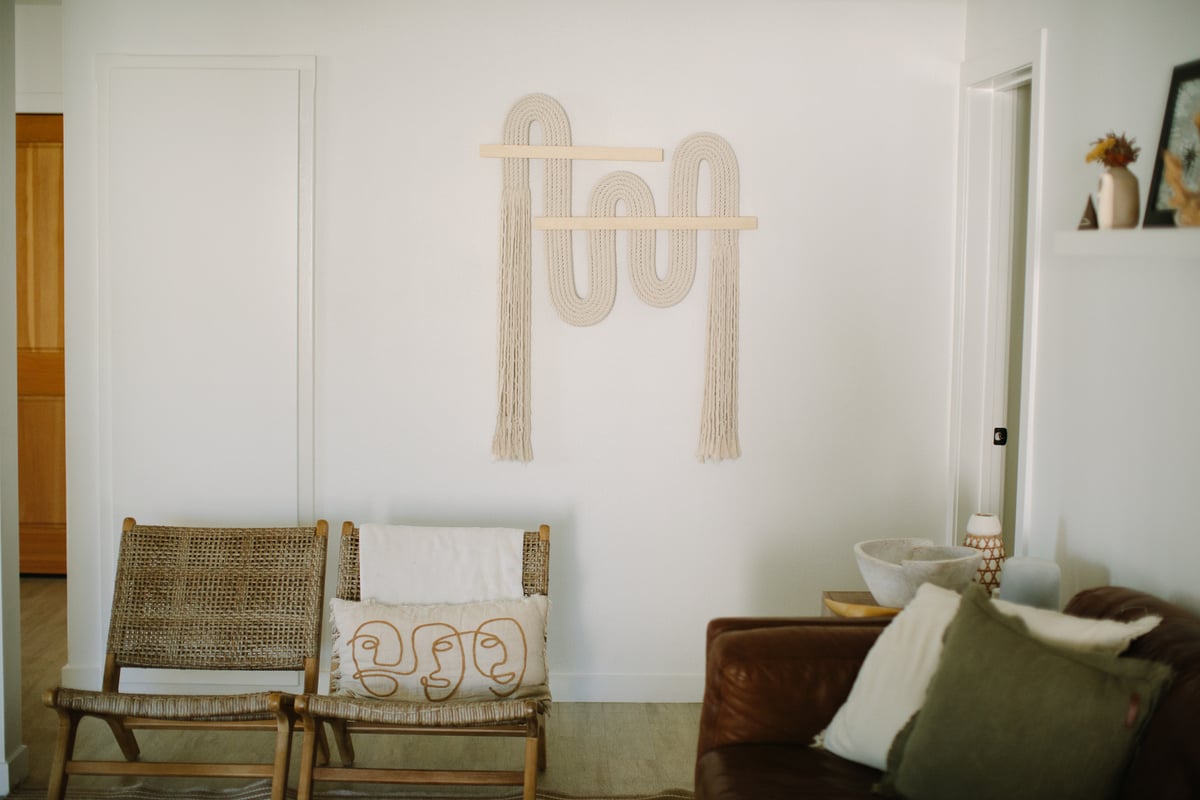 A quiet sitting area with two rattan chairs, a leather couch, and a macramé wall hanging — a warm therapy space.